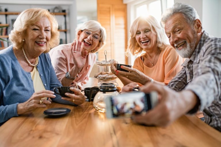 Group of happy seniors using smart phone and taking selfie while drinking teat at home.