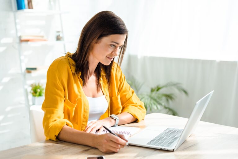 young woman working on laptop and writing in home office