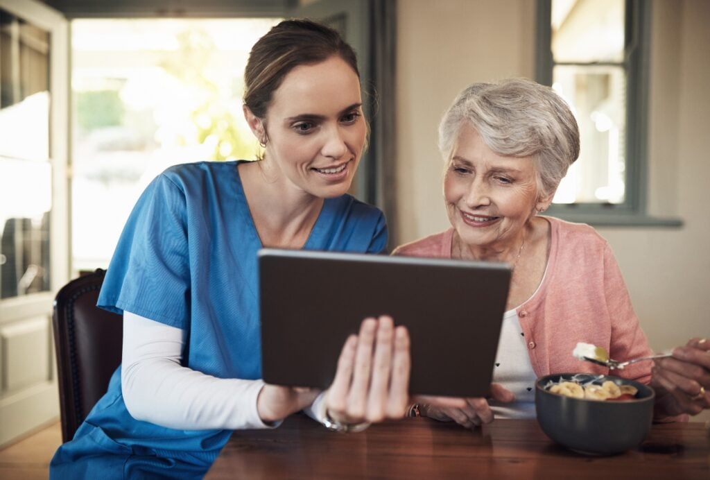 female caregiver holding a table device while showing the software to female elderly client
