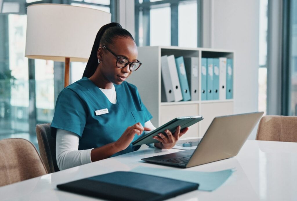 woman caregiver typing and entering data on a tablet device and computer, concept of data management