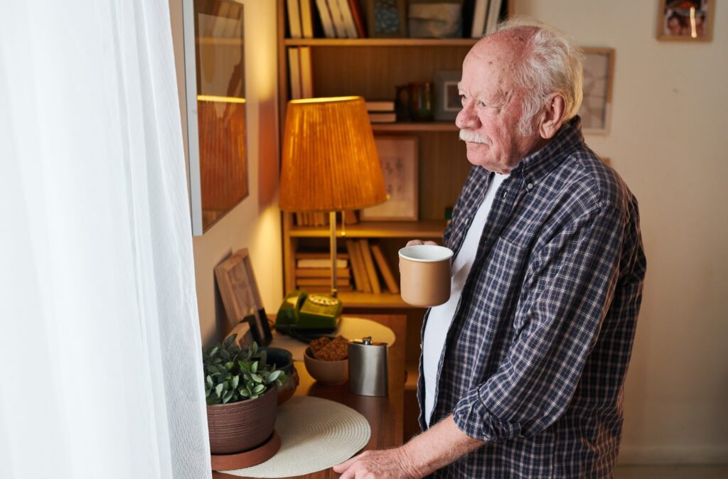 Senior man with mug of tea standing in front of window