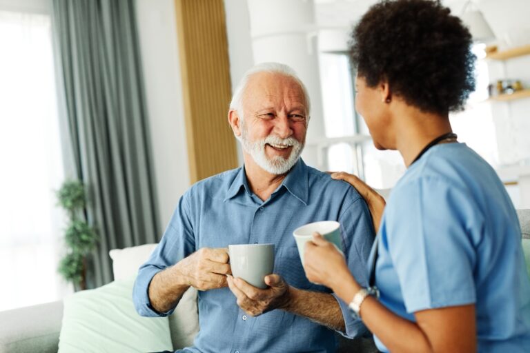 elderly man drinking coffee and smiling with caregiver at home