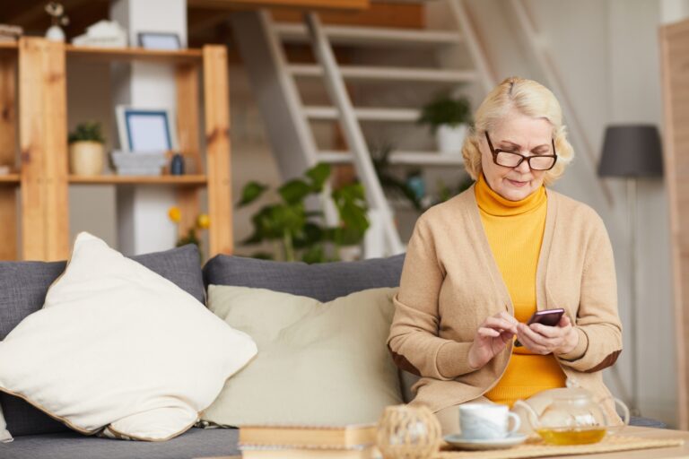 senior woman sitting alone at home while using mobile phone, concept of solo agers