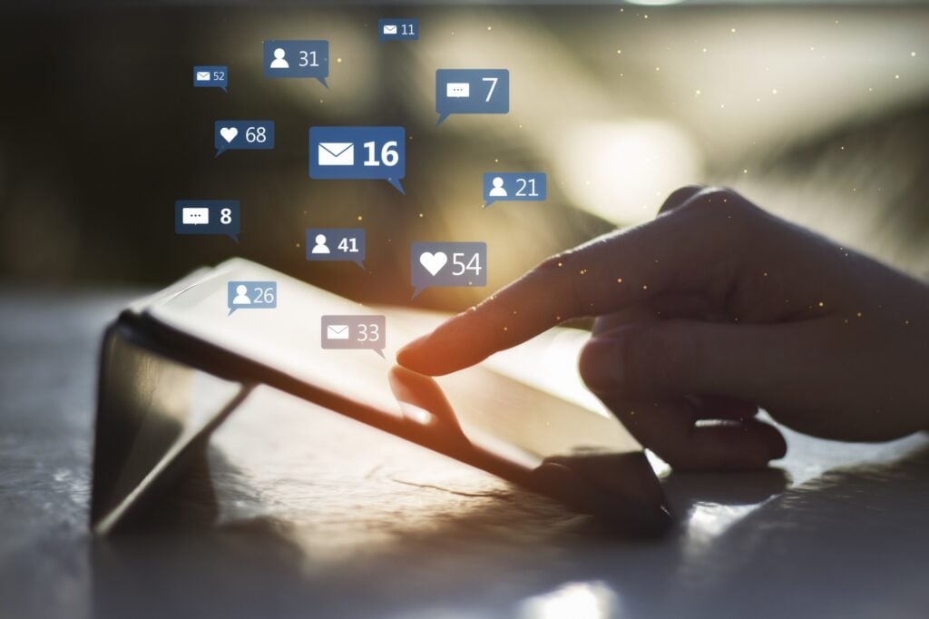 close up shot of hand using tablet device, social media icons hovering above