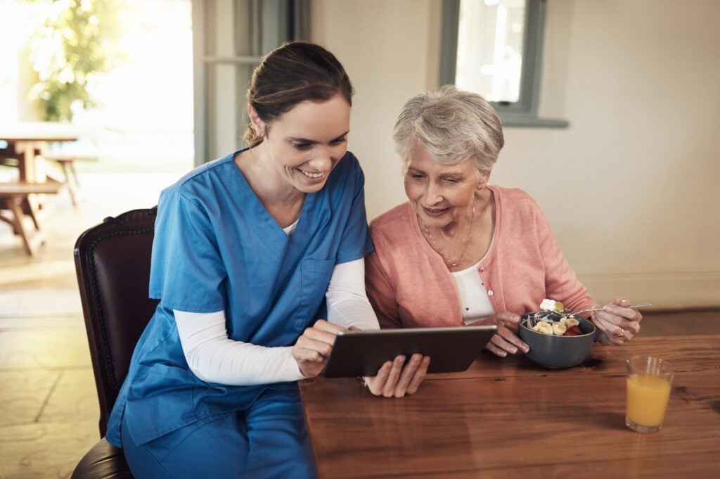 caregiver and senior woman using a digital tablet at breakfast time in a nursing home