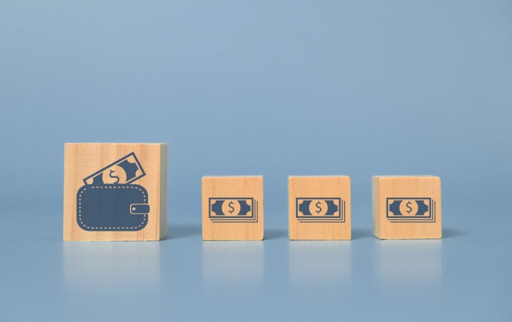 Wooden blocks displaying icons of a wallet and money stand on a blue surface