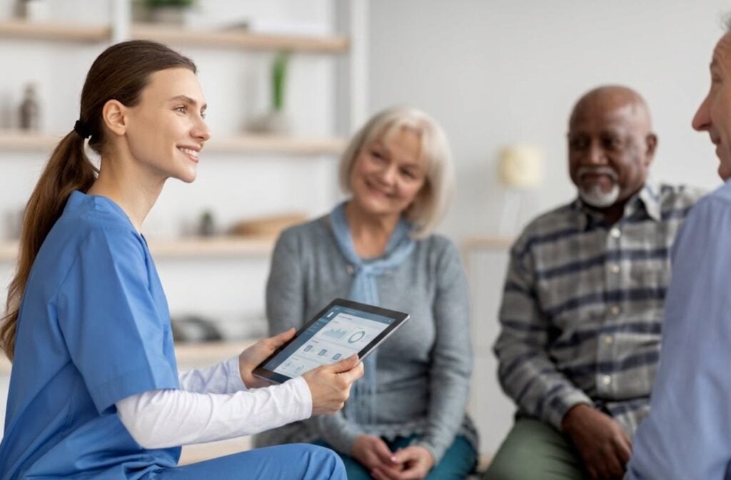caregiver speaking to elderly patient and family while holding tablet device