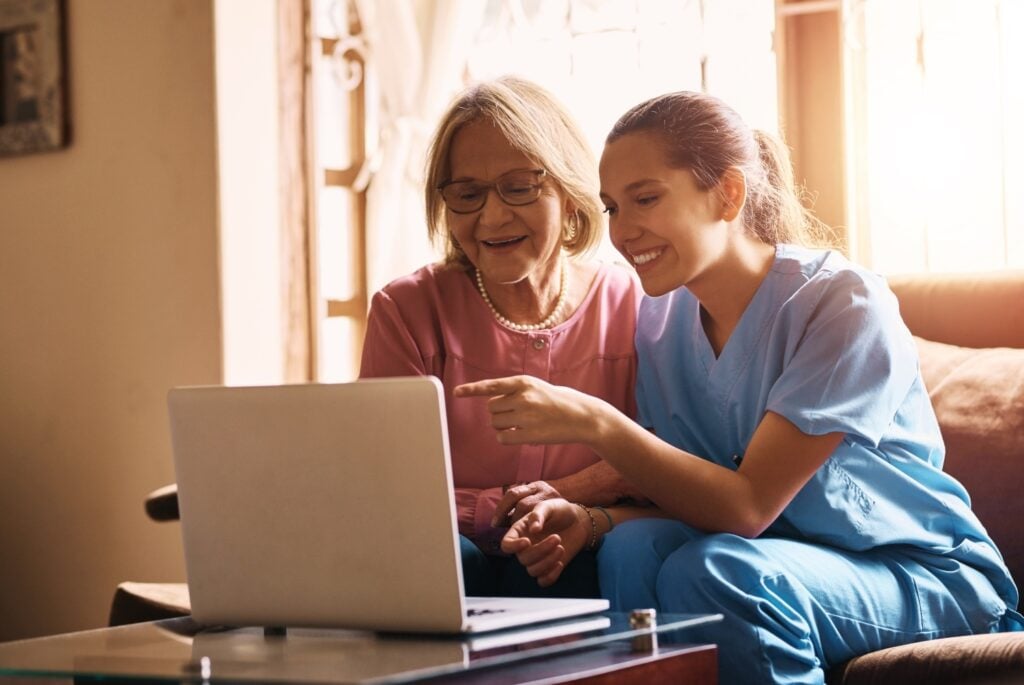 elderly woman and female caregiver using laptop to update family members, concept of coordination