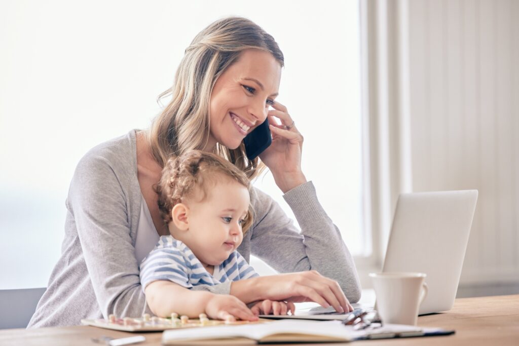 mother smiling as she talks on phone while toddler sits in her lap
